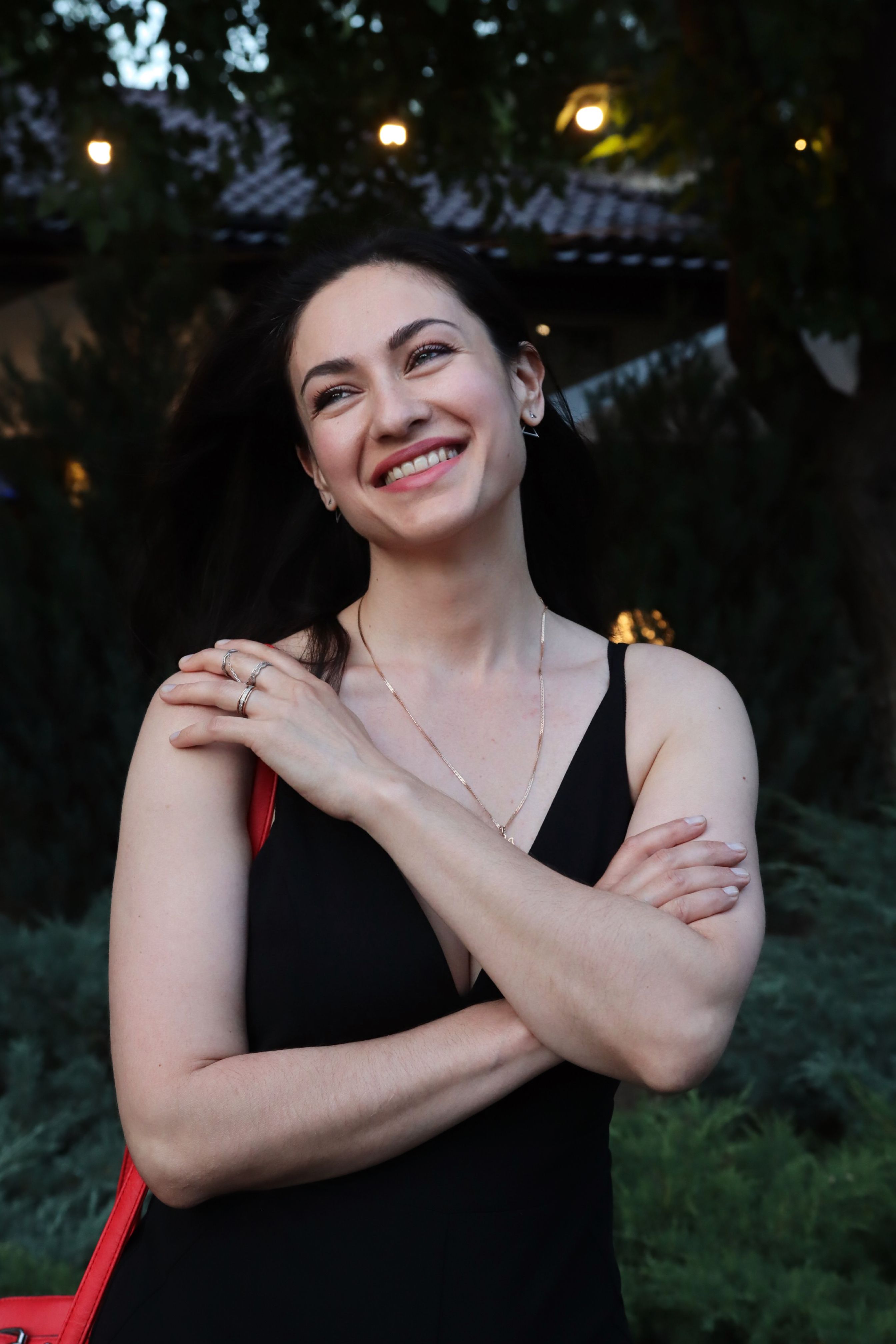 A joyful woman smiling outdoors with greenery in the background.