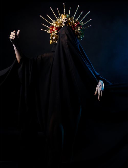 Free A mysterious figure in a black cloak with a vibrant ornate headpiece in a dark setting. Stock Photo