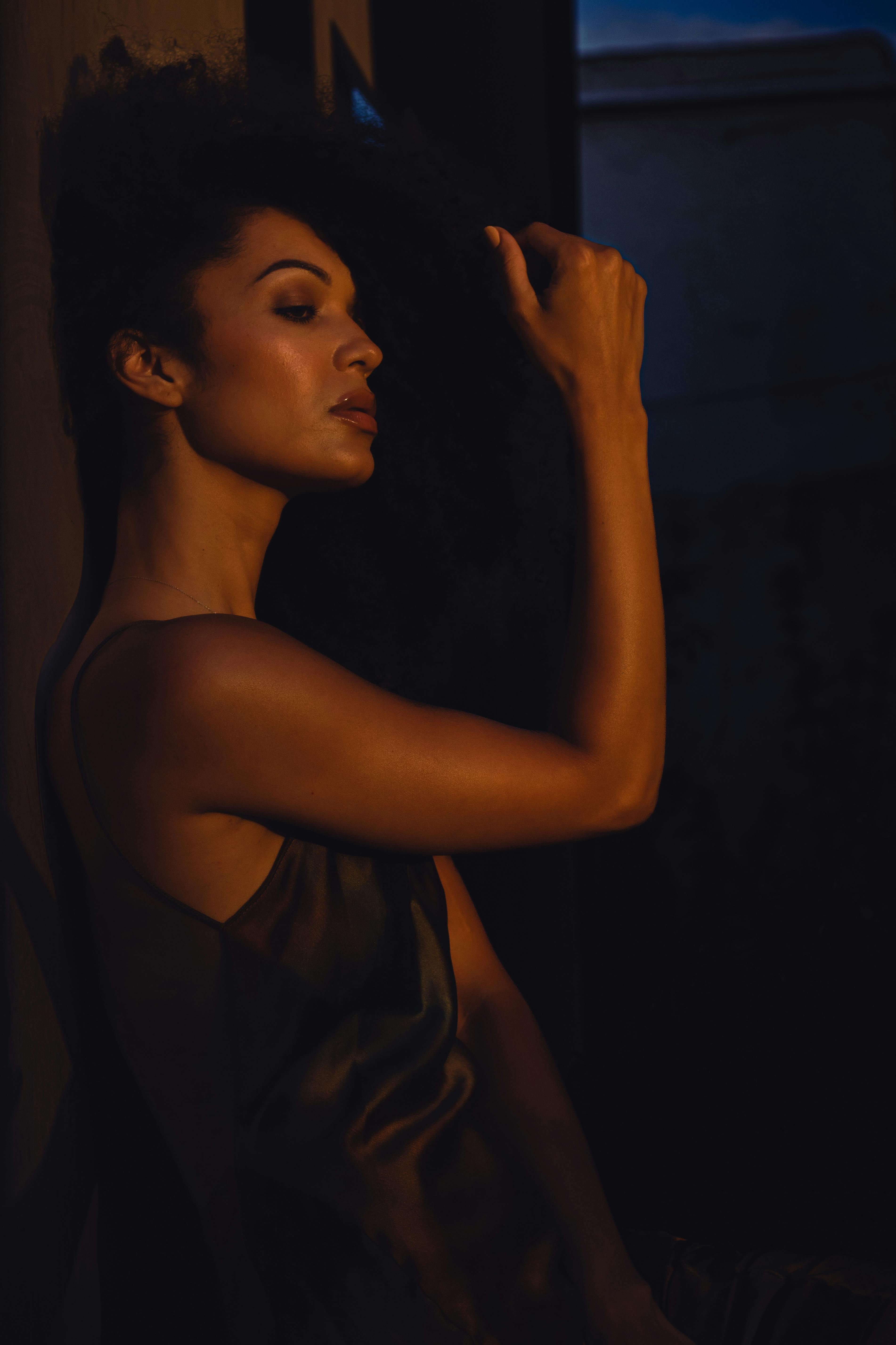 Silhouette of woman leaning against wall in dim light, moody atmosphere.