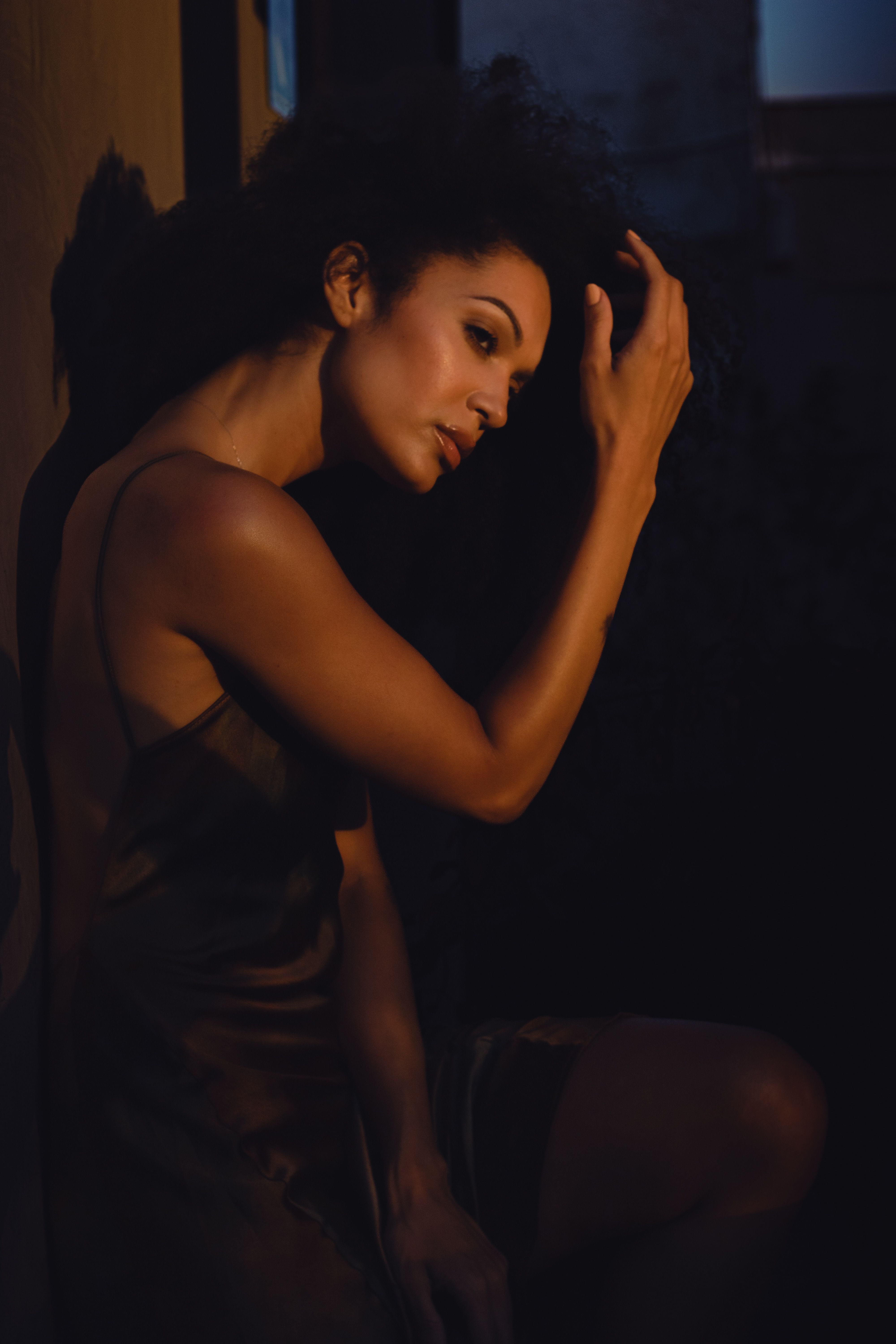 A thoughtful woman in dim, warm lighting, creating a moody atmosphere.