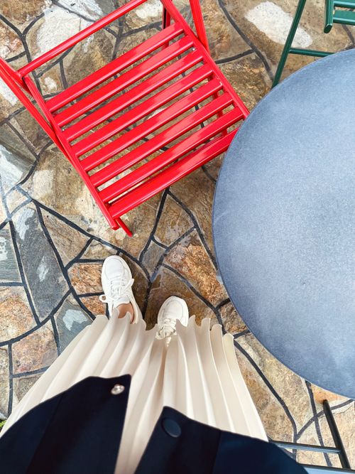 Free Top-down view of white sneakers, pleated skirt, and a red chair on textured stone flooring. Stock Photo