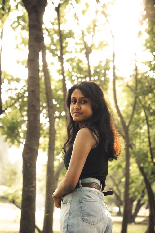 Free A serene woman standing outdoors in a sunlit park surrounded by lush green trees. Stock Photo