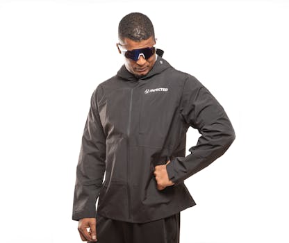 Model wearing a black all-weather sports jacket with sunglasses against white background.