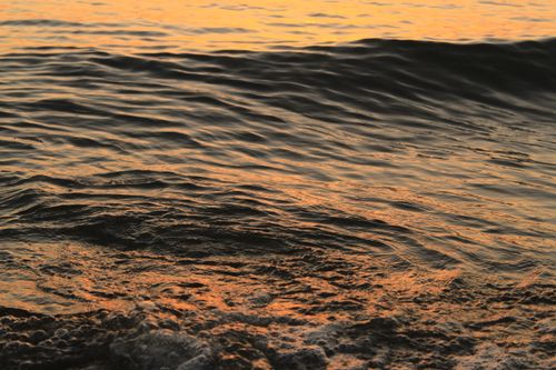 Free Peaceful ocean waves reflecting the warm colors of a sunset, creating a calming atmosphere. Stock Photo