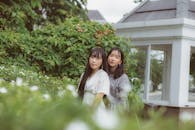 两名亚洲女性身着时尚服装，在户外郁郁葱葱的绿树丛中摆姿势