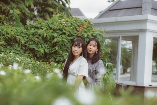 两名亚洲女性身着时尚服装，在户外郁郁葱葱的绿树丛中摆姿势