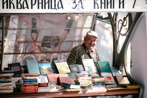 Free A cheerful street vendor selling books at an outdoor stall in Skopje, North Macedonia. Stock Photo