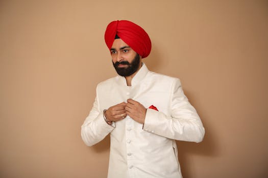 Portrait of a Sikh man wearing a white sherwani and red turban, buttoning jacket.