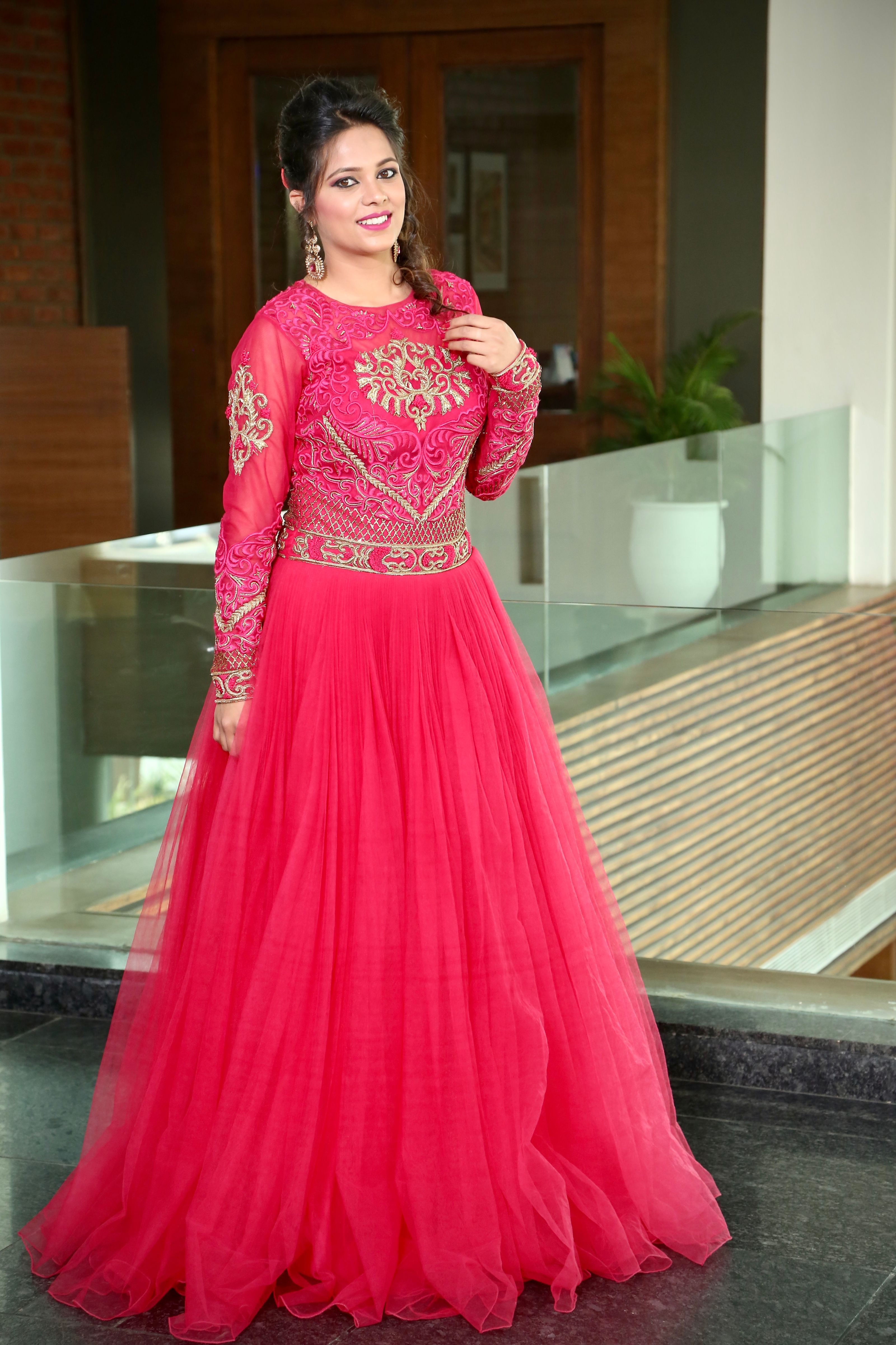 Mulher usando um vestido tradicional rosa vibrante dentro de casa, sorrindo com confiança.