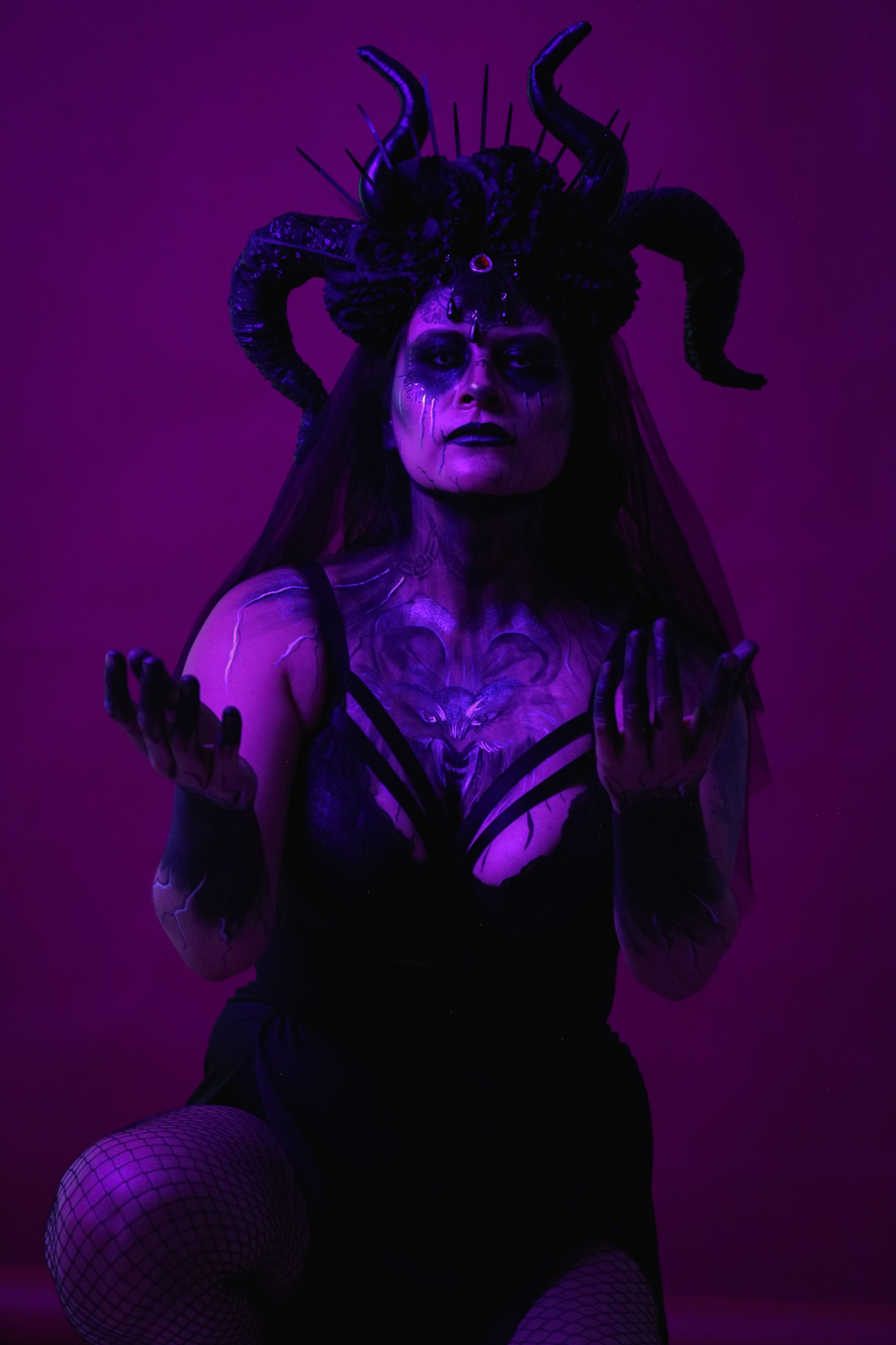 Dark fantasy portrait of a woman with horns and body paint under purple lighting.
