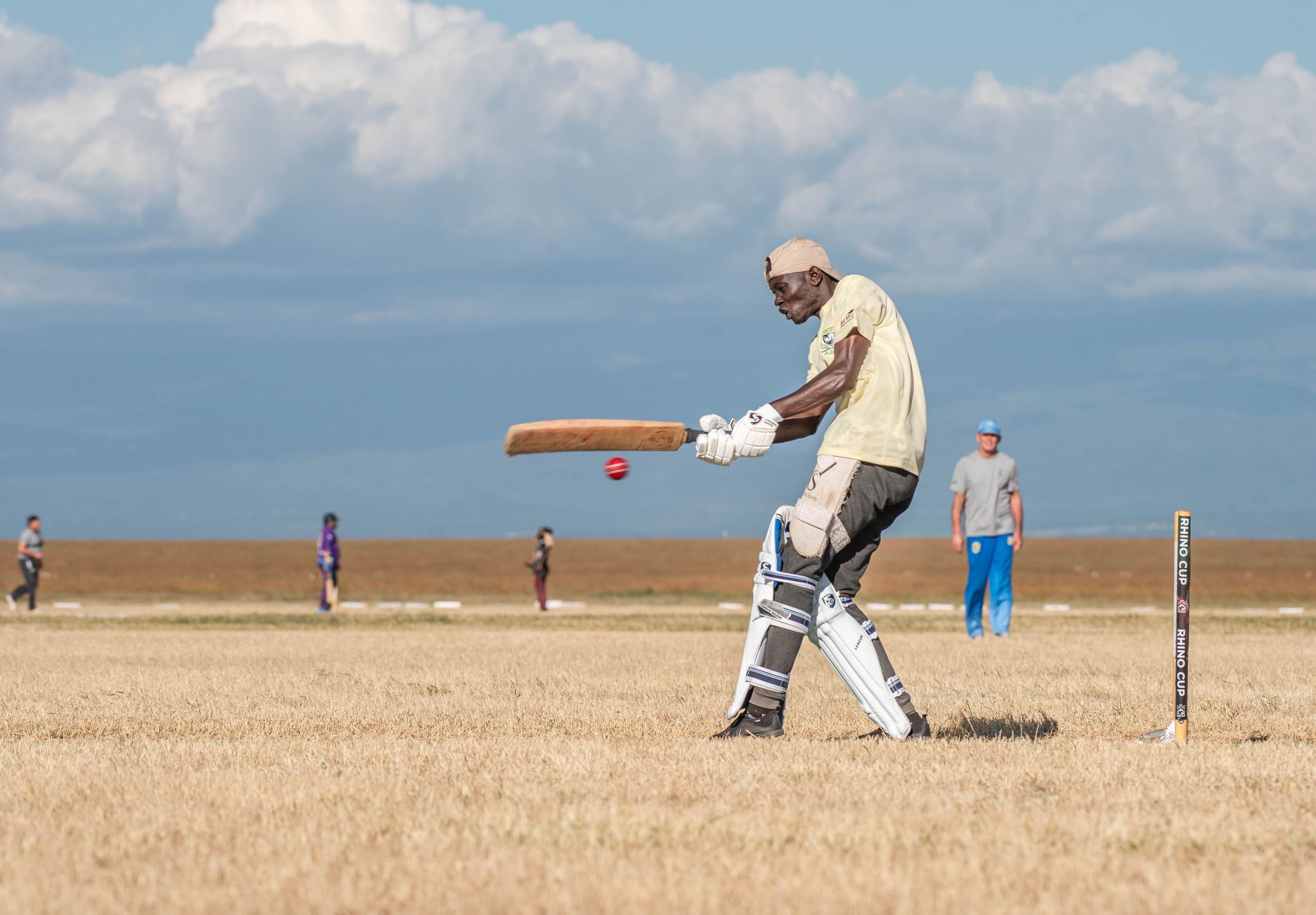Elderly man batting in a cricket match on a sunny field.