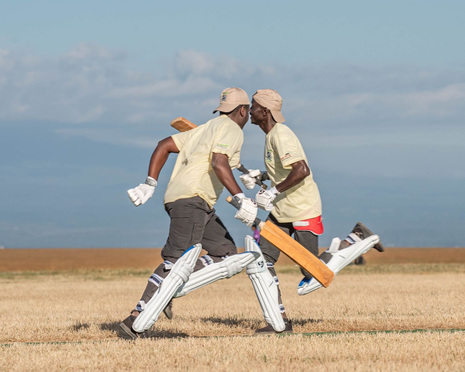 Two cricketers sprint on field, bats in hand, showing dynamic sports action.
