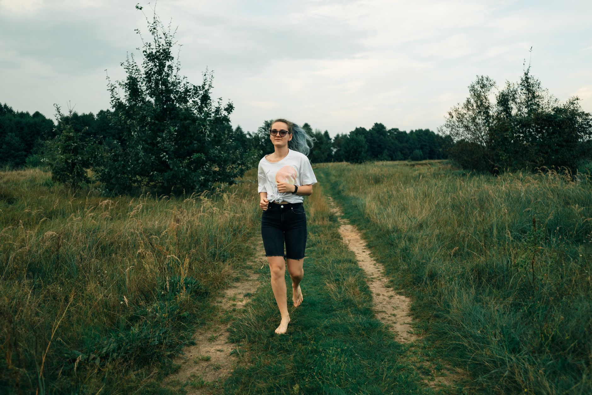Barefoot woman walking on a grassy path in a rural area on a summer day.