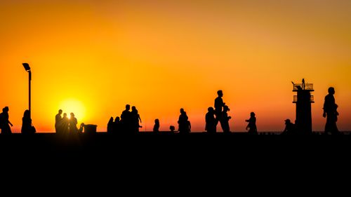 Free Silhouetted people walking against a vibrant sunset with warm orange hues in the sky. Stock Photo