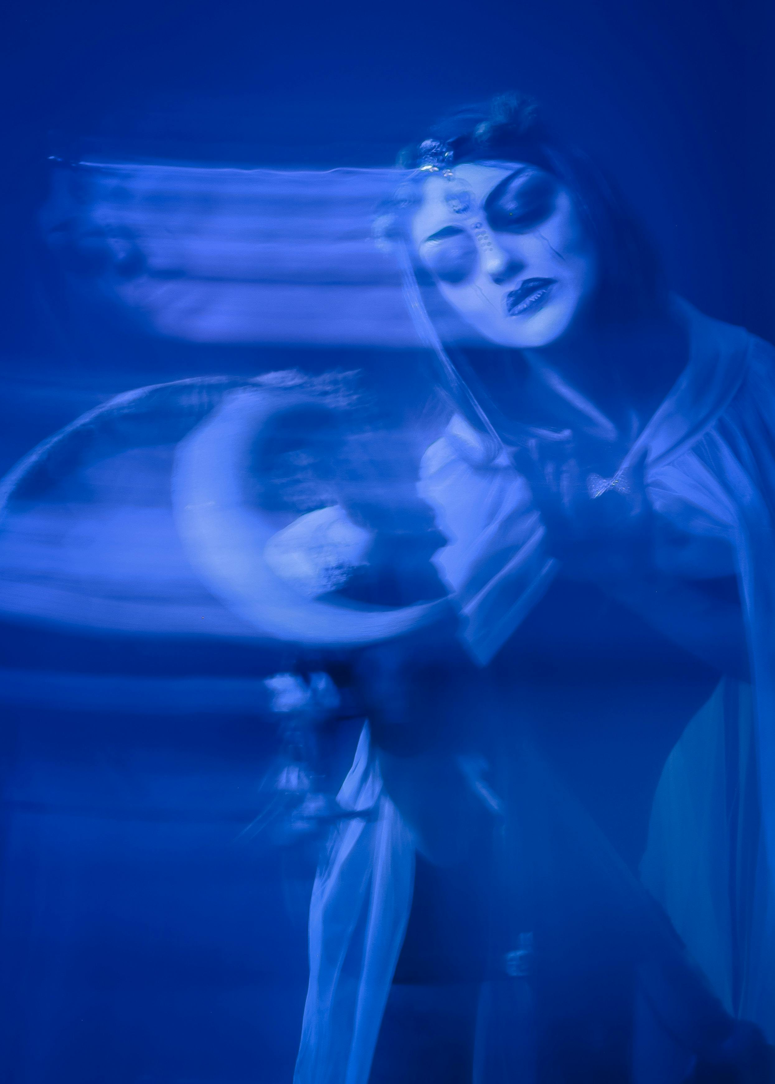 Ethereal portrait of a woman with blurred motion effect in mystical blue tones, creating a dreamlike atmosphere.