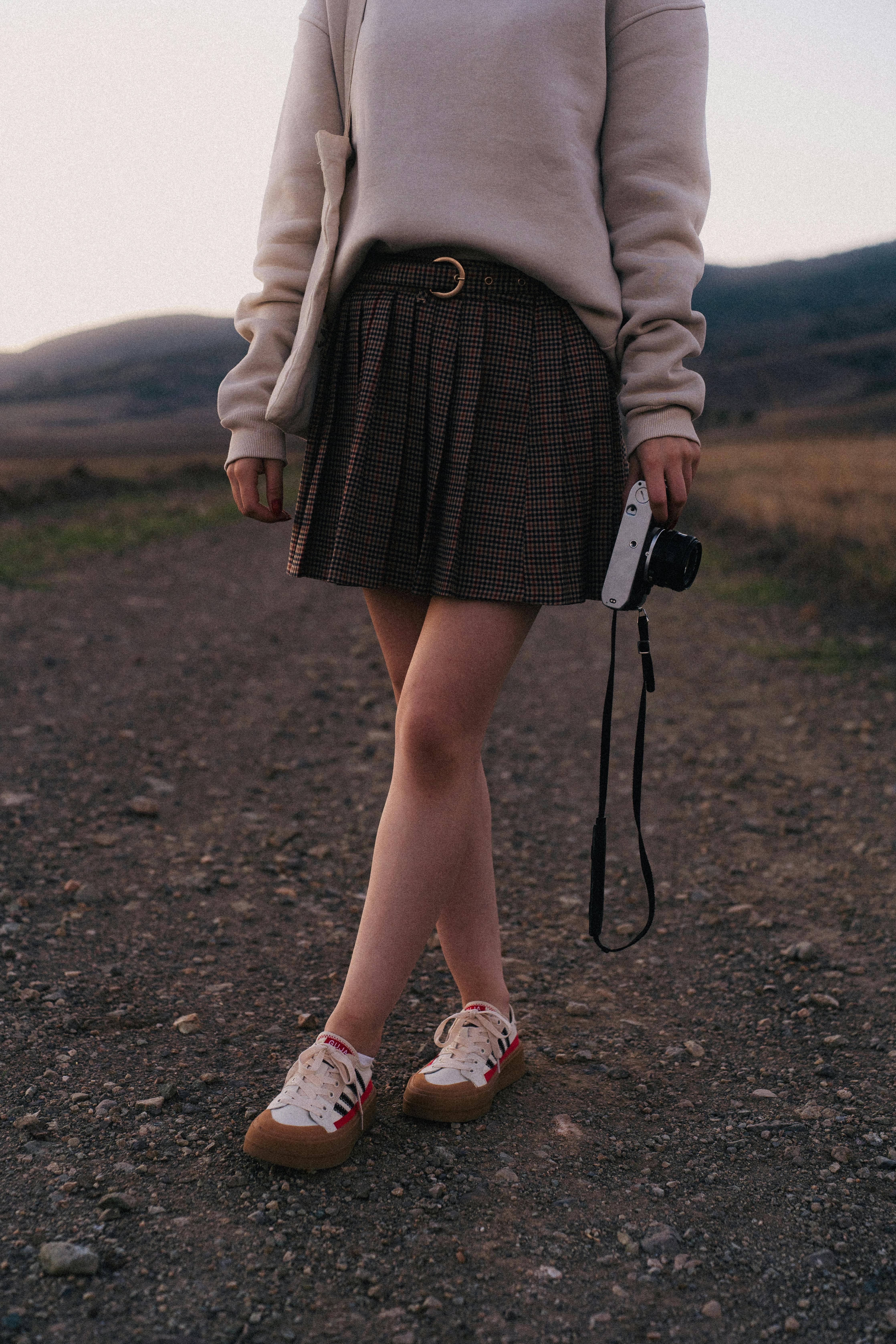 Woman in casual attire holding a camera outdoors during twilight.