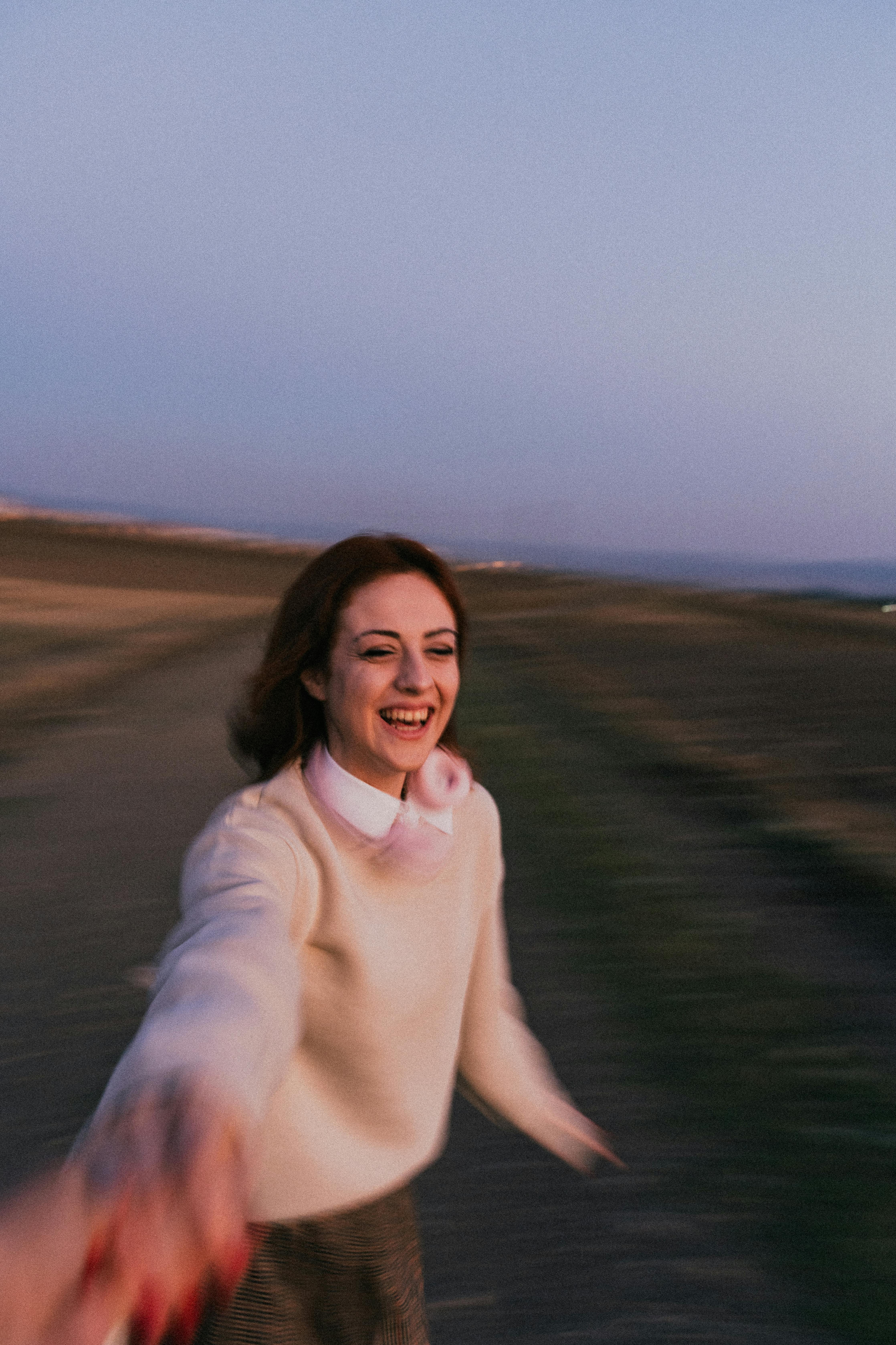 A smiling woman running joyfully outdoors during sunset, holding a hand.