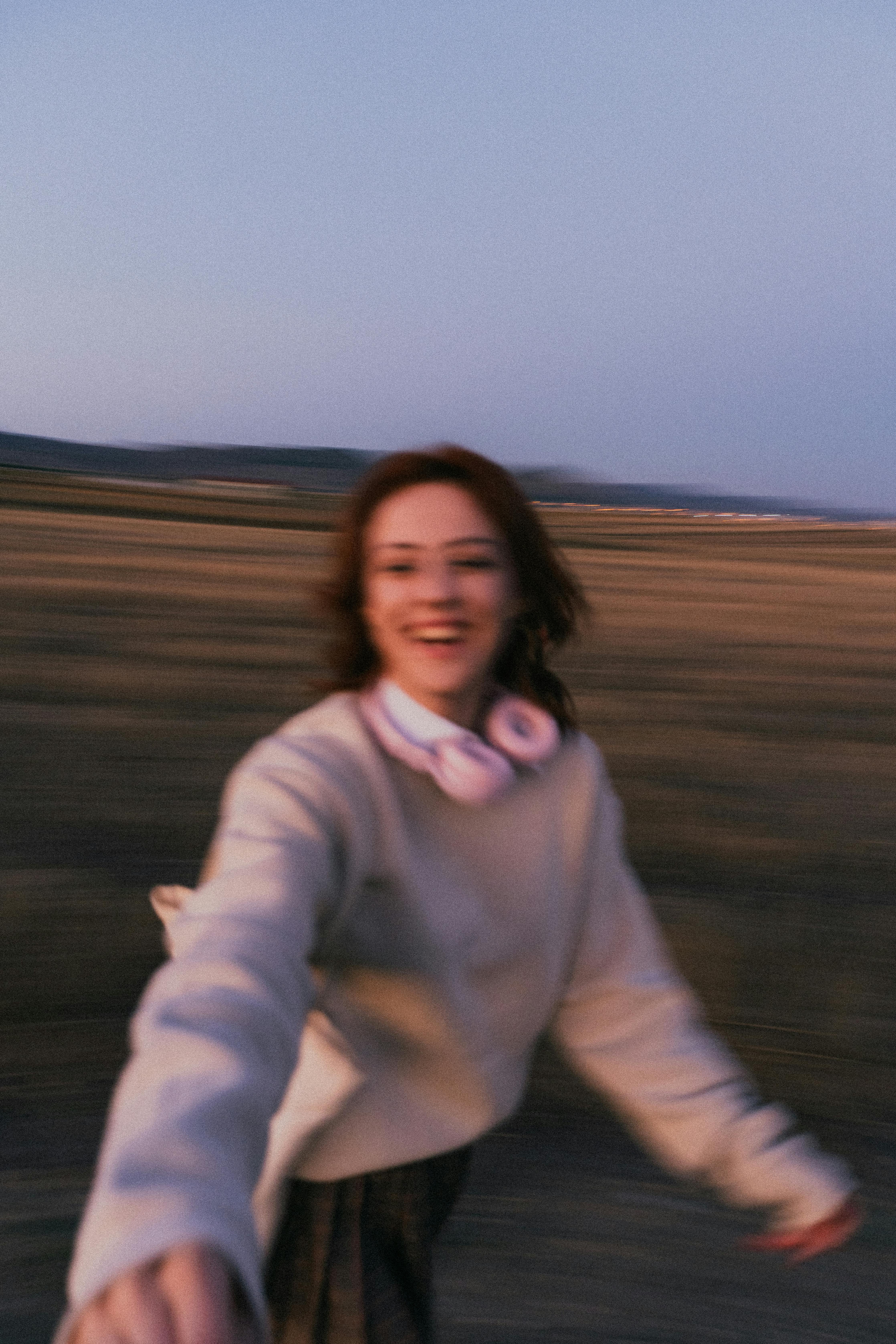 A young woman smiling and moving energetically in an open field during twilight.