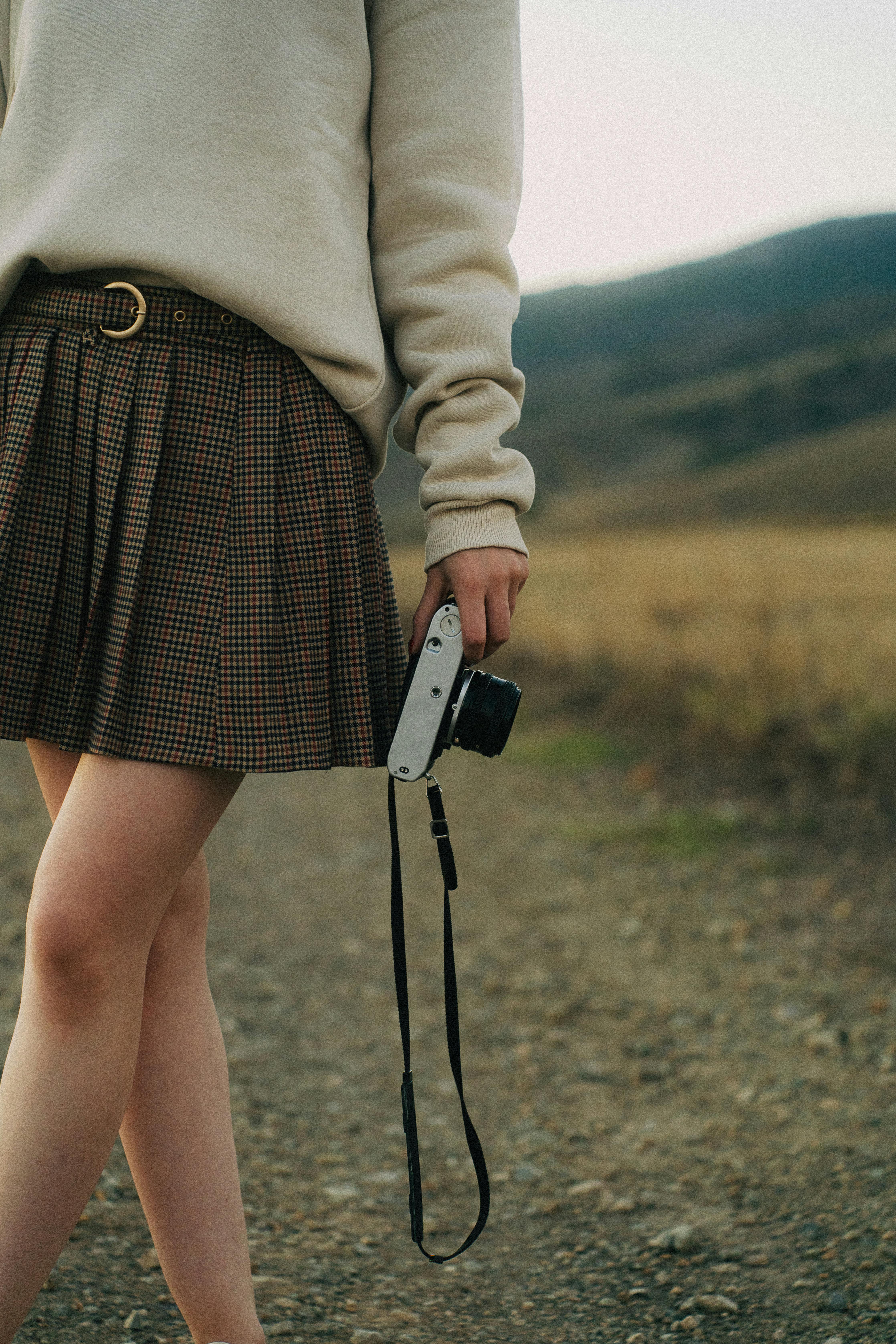 A stylish young woman in autumn attire holding a vintage camera in an outdoor setting.