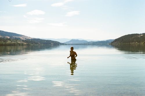 Free A person enjoying a peaceful swim in a calm lake surrounded by mountains. Stock Photo