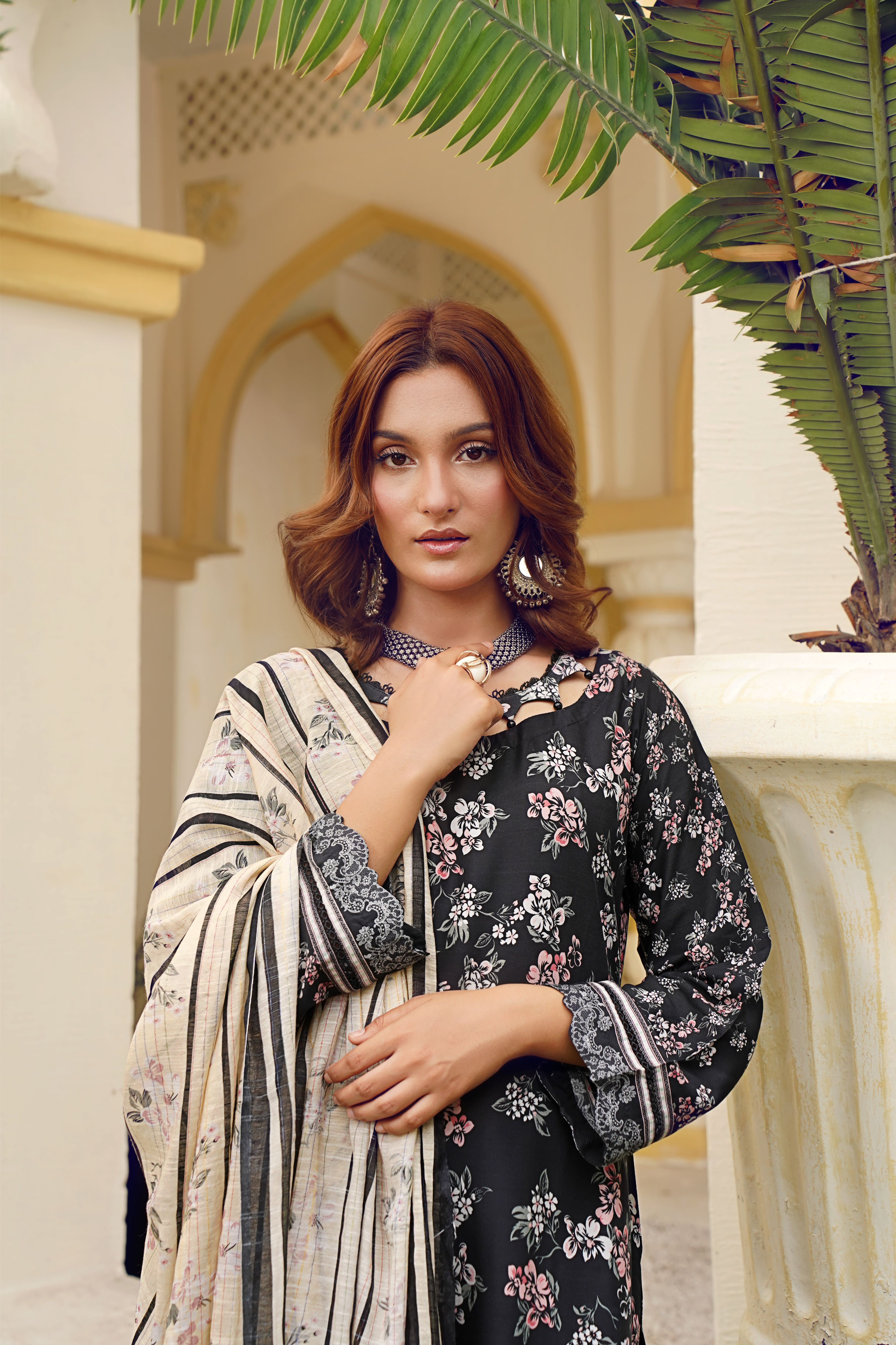 A graceful woman in traditional floral attire poses with elegance against architectural backdrop.