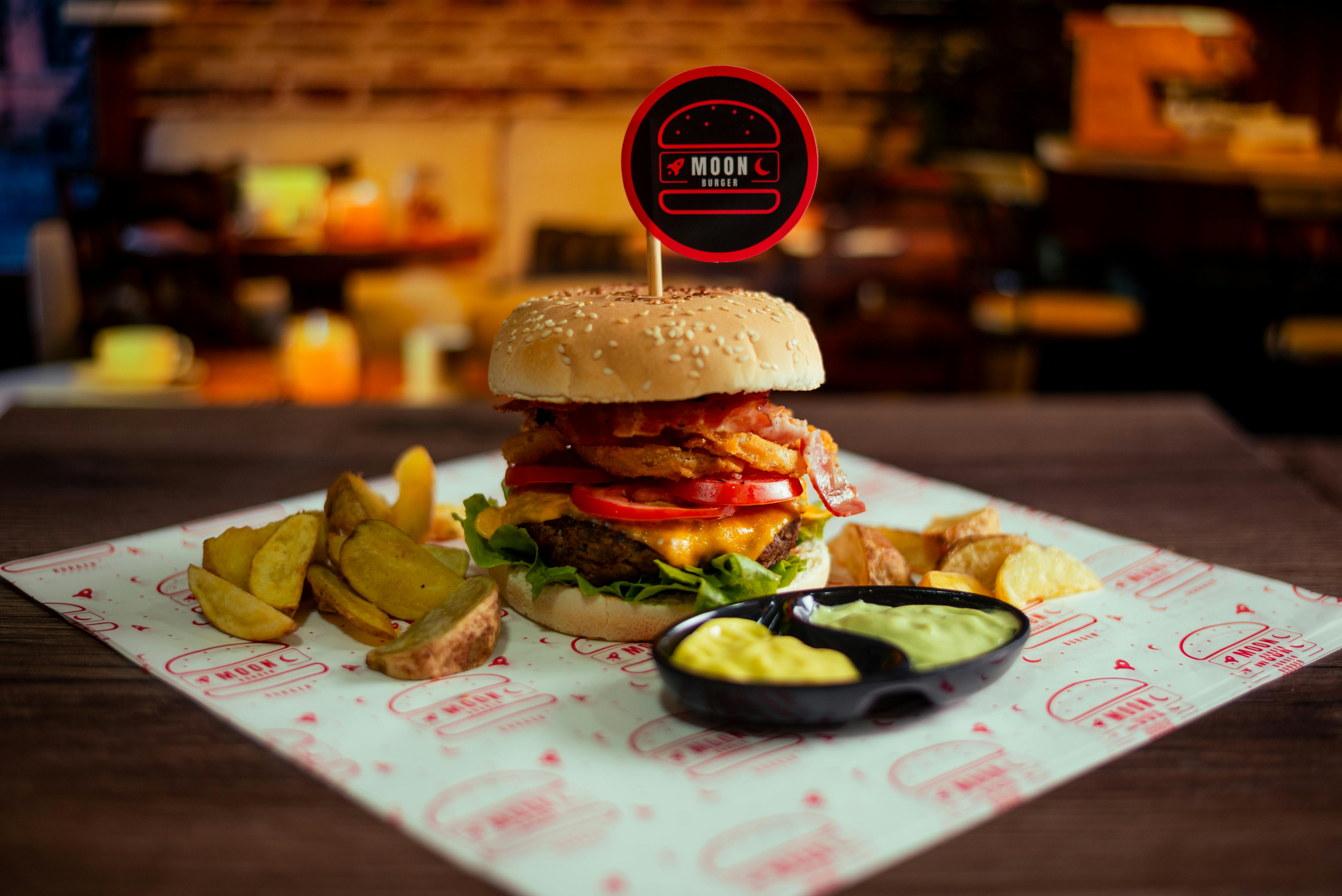 A juicy gourmet burger with fries on a wooden table in a cozy restaurant setting.
