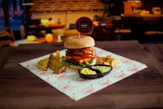 A mouth-watering gourmet burger with crispy wedges and sauce in a cozy restaurant setting.