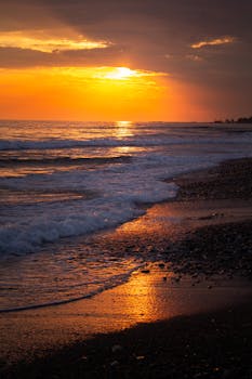 A mesmerizing sunset over the ocean with waves gently lapping the sandy shore.