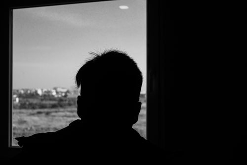 Free Black and white silhouette of a person gazing out an indoor window to a distant cityscape. Stock Photo