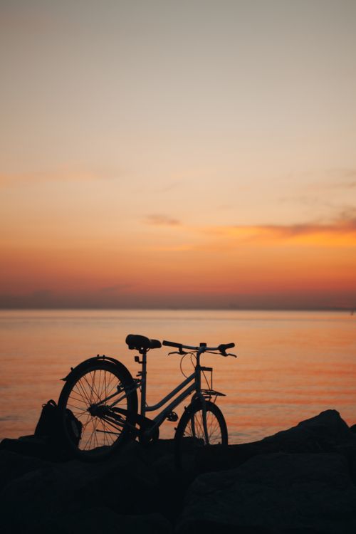 Free A tranquil sunset with a bicycle silhouette by the ocean, perfect for lifestyle and travel themes. Stock Photo