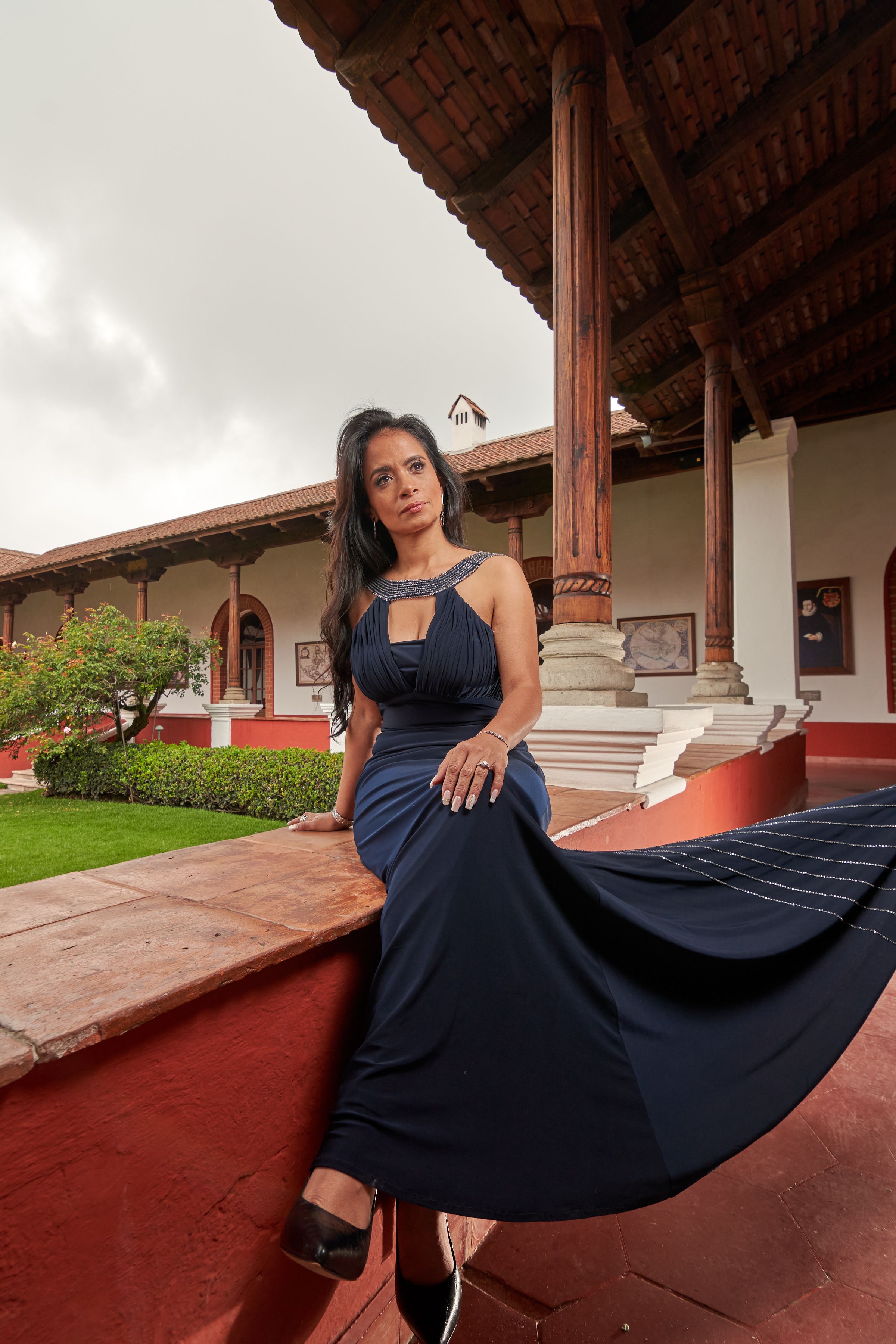 A woman in a navy dress poses in a vibrant historic courtyard setting, showcasing elegance.