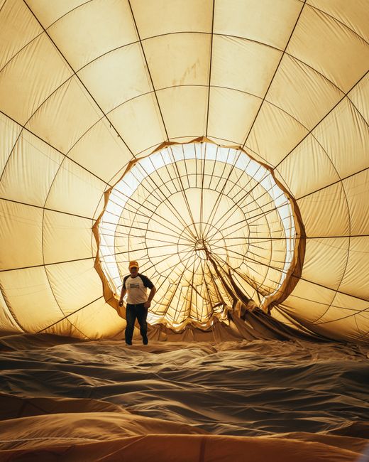 A man stands inside a deflated hot air balloon, preparing for takeoff.