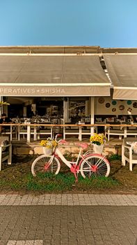 A delightful scene of a vintage pink bicycle adorned with yellow flowers outside a cozy café.