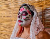 Close-up portrait of a woman with vibrant Dia de los Muertos face paint and lace veil indoors.