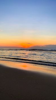 Serene sunset over a calm beach, waves gently lapping the shore under a colorful sky.