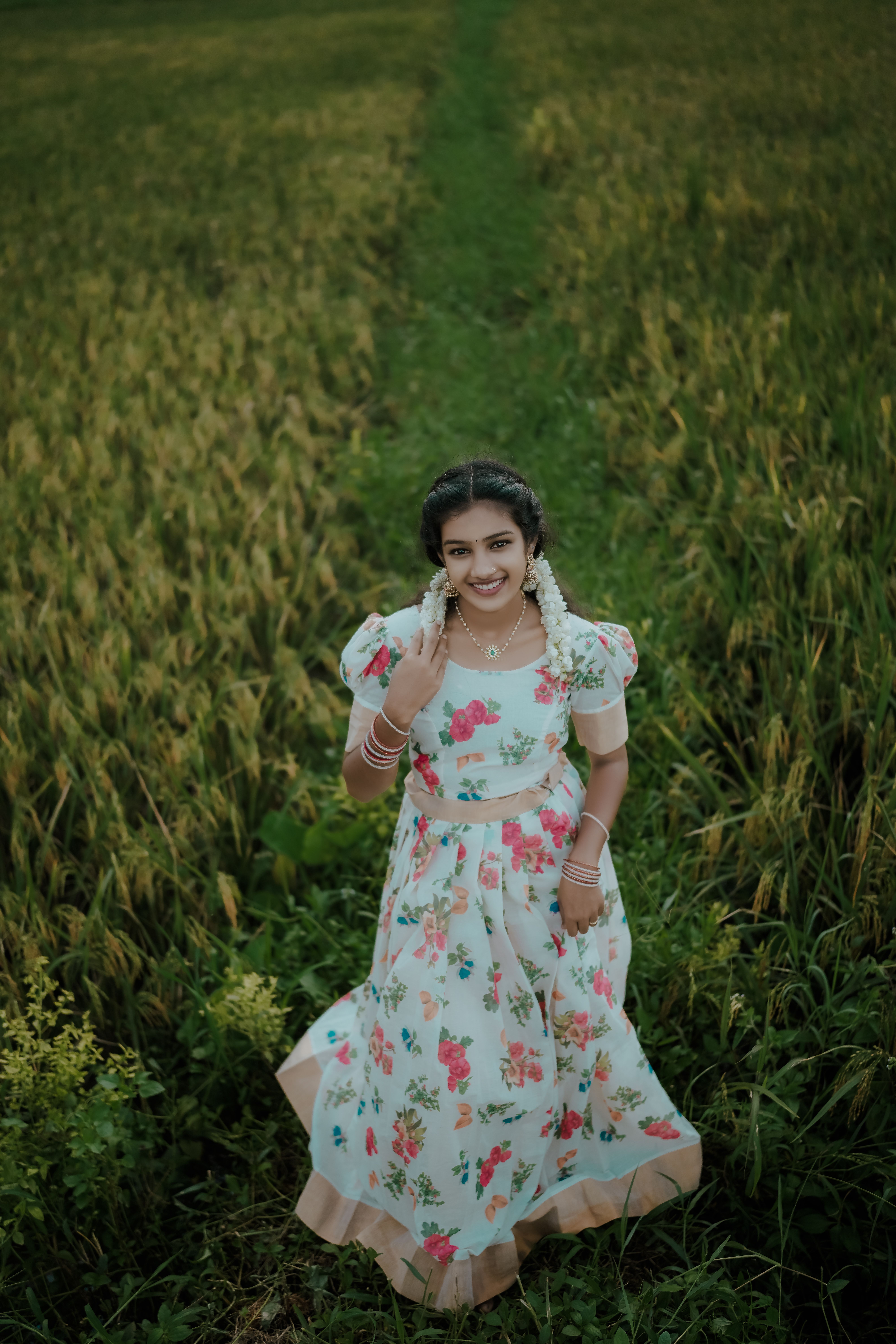 Young woman in floral dress enjoying a walk through a lush green field, smiling.