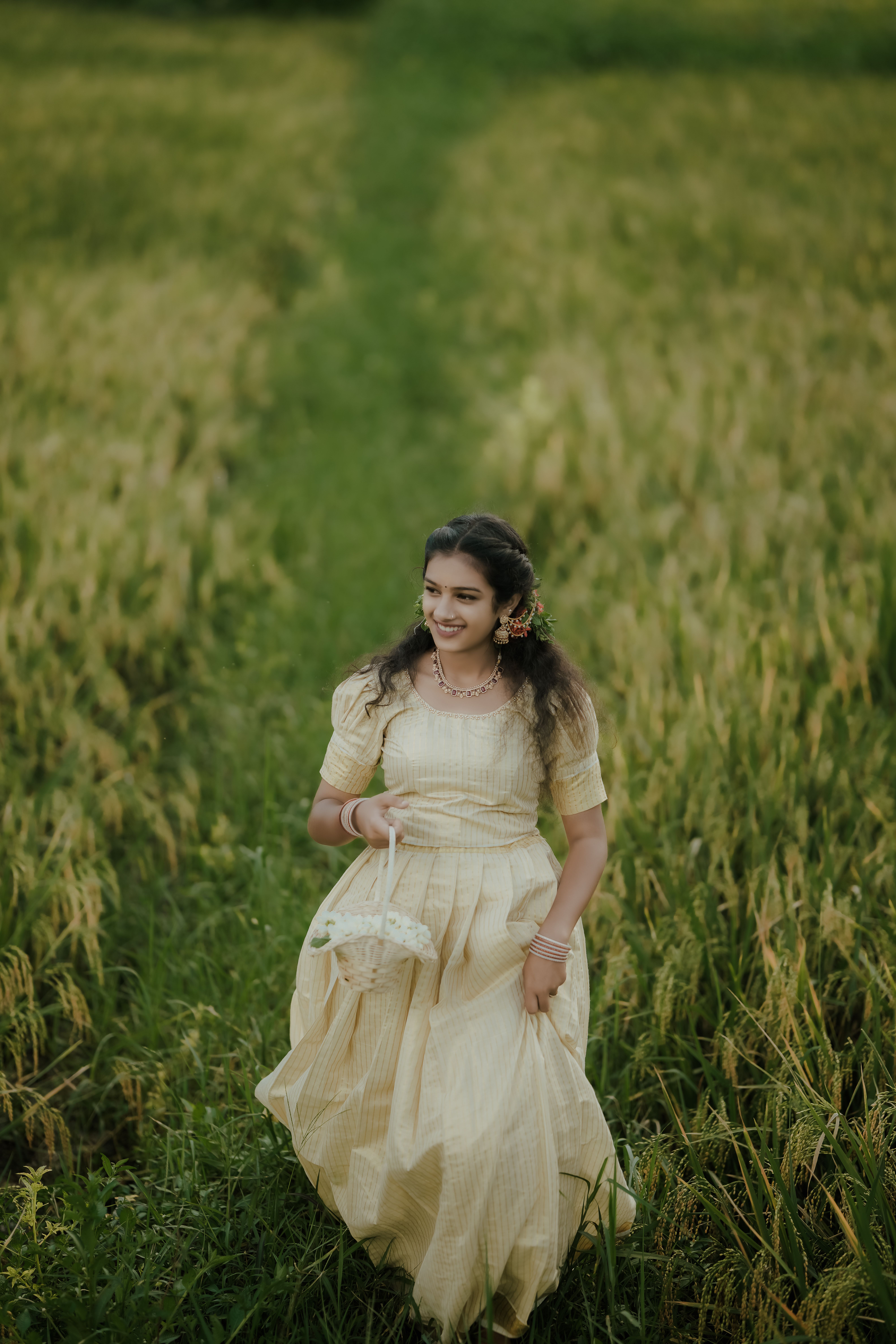 Smiling woman in a flowing dress walking through a green field outdoors.