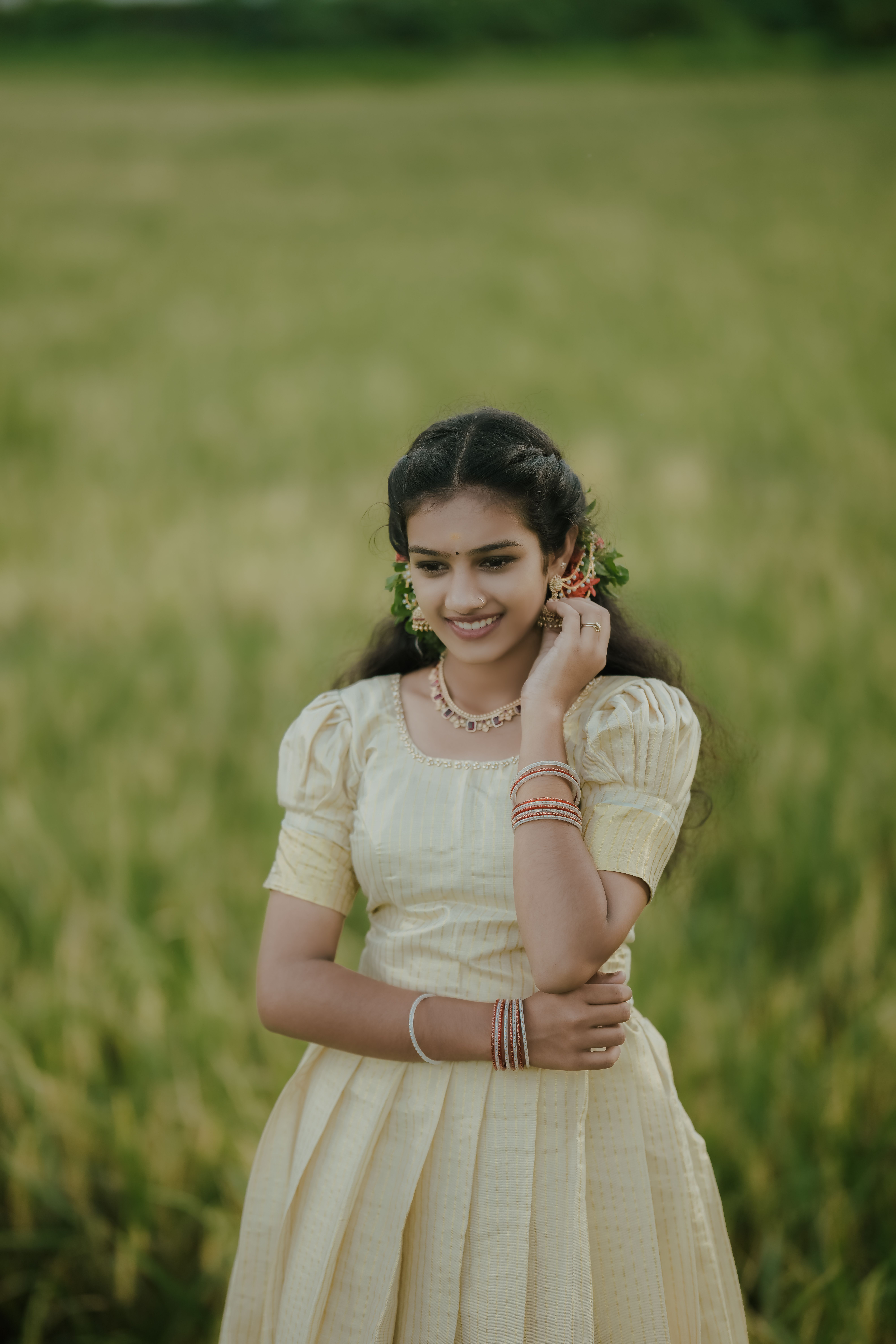 Young woman in yellow dress standing in a lush green field, smiling happily.