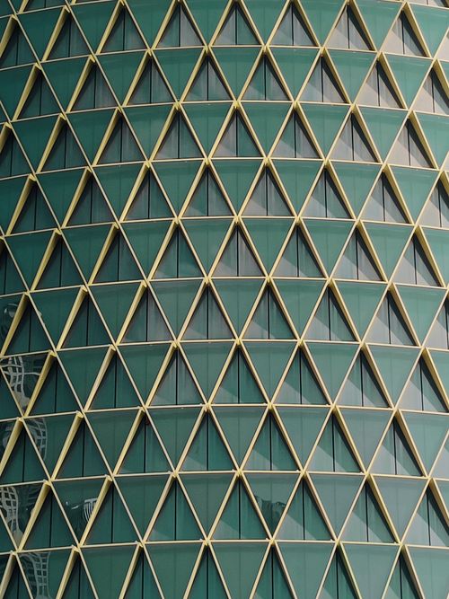 Free Close-up of a modern skyscraper with a geometric facade pattern in sunlight. Stock Photo