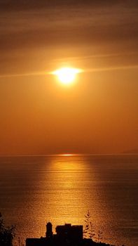 Golden sunset reflecting on calm ocean with silhouette of buildings in foreground.