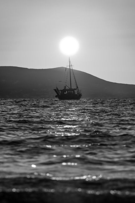 Monochrome sailboat silhouette against the sunrise in Naxos, Greece.