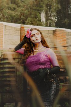A woman in vibrant costume and skull makeup poses gracefully outdoors.