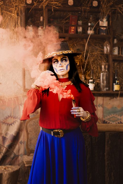 Free Masked woman in vibrant costume celebrating Day of the Dead with decorative makeup in a rustic setting. Stock Photo