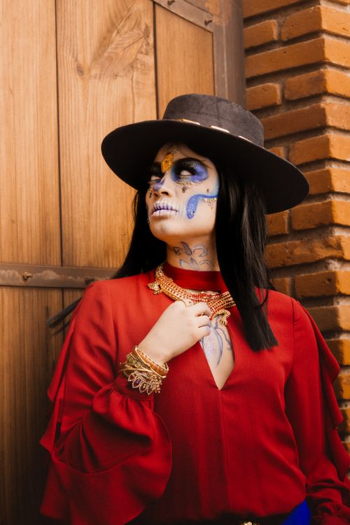 Free A woman with artistic Day of the Dead makeup wearing a vibrant red dress and black hat. Stock Photo