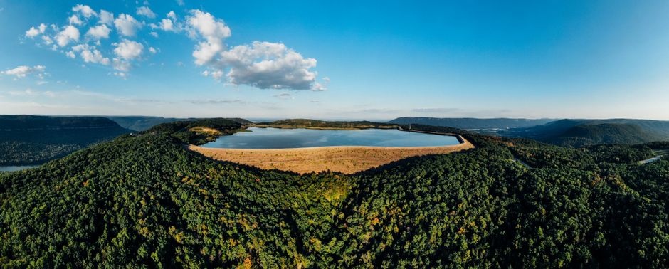 A stunning aerial photo capturing a tranquil lake surrounded by lush forested hills under a clear blue sky.