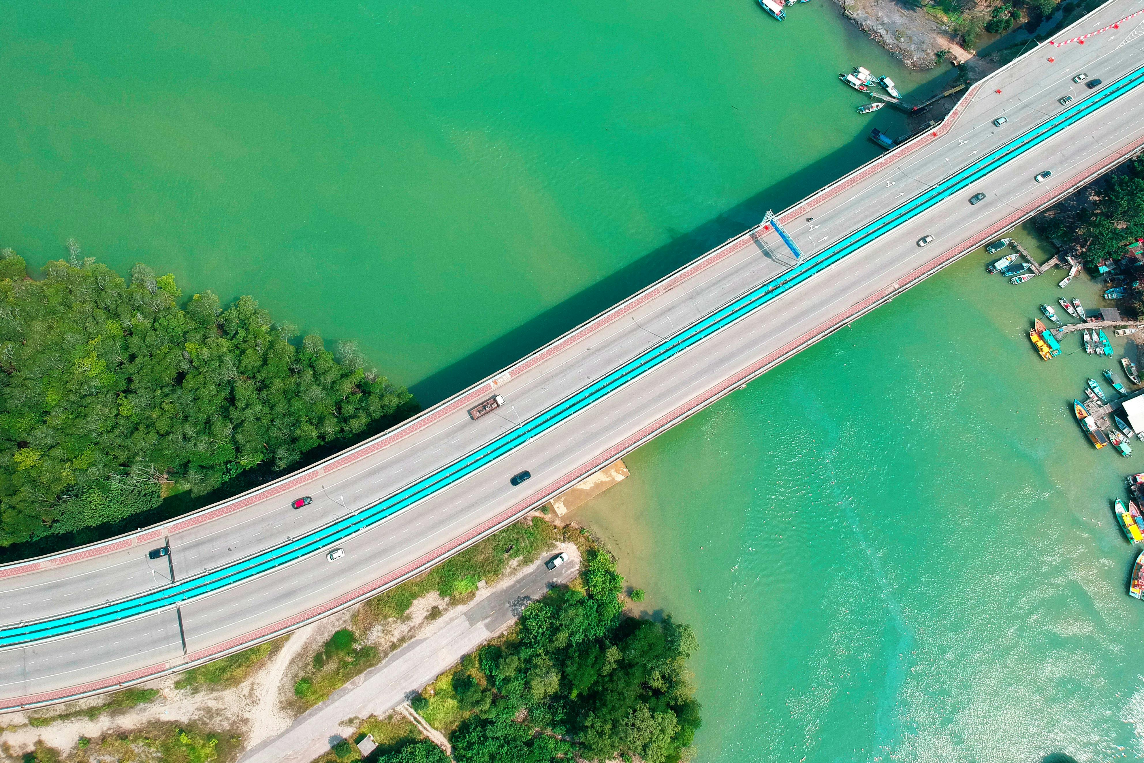 Aerial shot of a bridge spanning over a turquoise water body with boats and lush greenery.