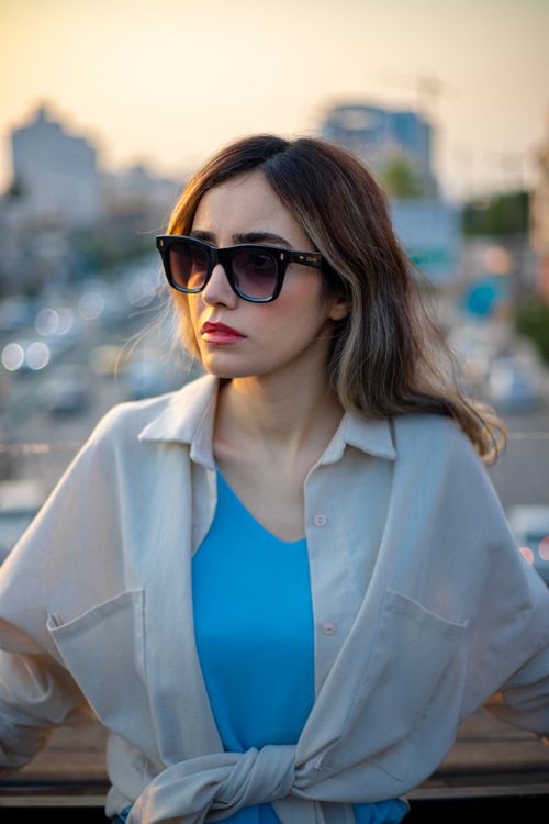 Free Woman wearing sunglasses with a cityscape at sunset, exuding urban fashion vibes. Perfect for lifestyle and fashion concepts. Stock Photo