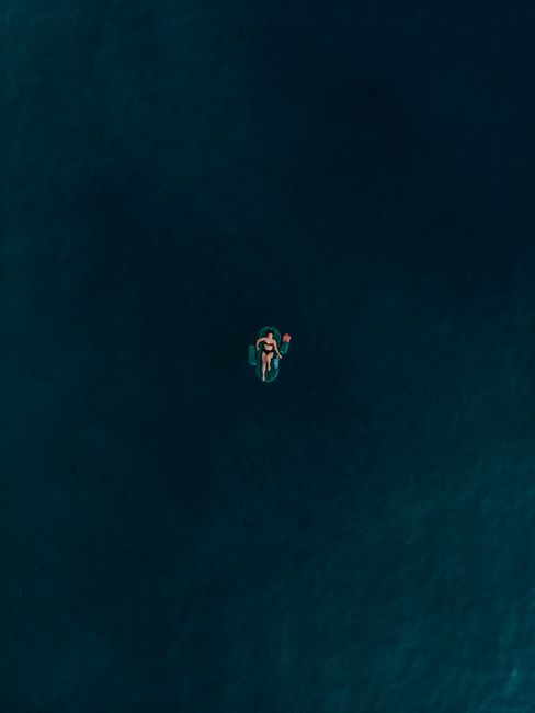A lone woman on an inflatable float relaxes in the vast blue ocean, creating a serene and peaceful scene.