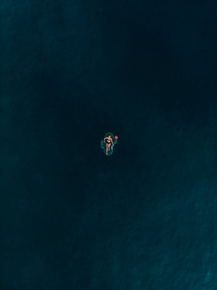 Aerial Photo Of Woman Lying On Inflatable Floater In The Middle Of Ocean