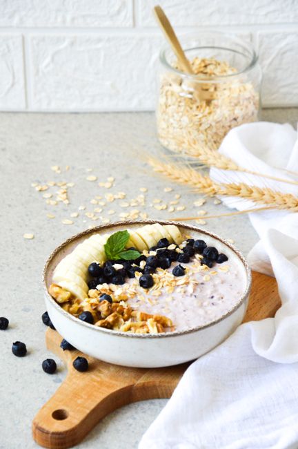 Delicious oatmeal breakfast bowl with banana, blueberries, and walnuts on a wooden board.